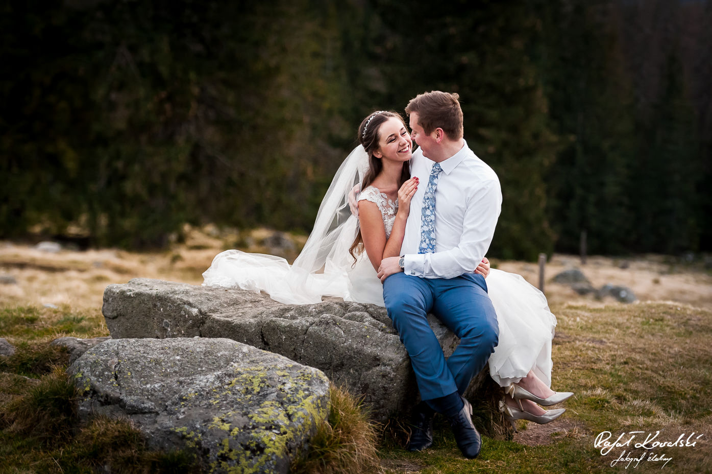 Plener ślubny w Górach - świeżo poślubieni małżonkowie pozują siedząc na wielkim kamieniu