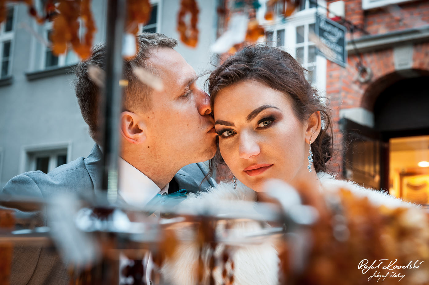 czuły pocałunek od pana młodego w blasku bursztynowej poświaty witryn na ulicy Mariackiej w Gdańsku