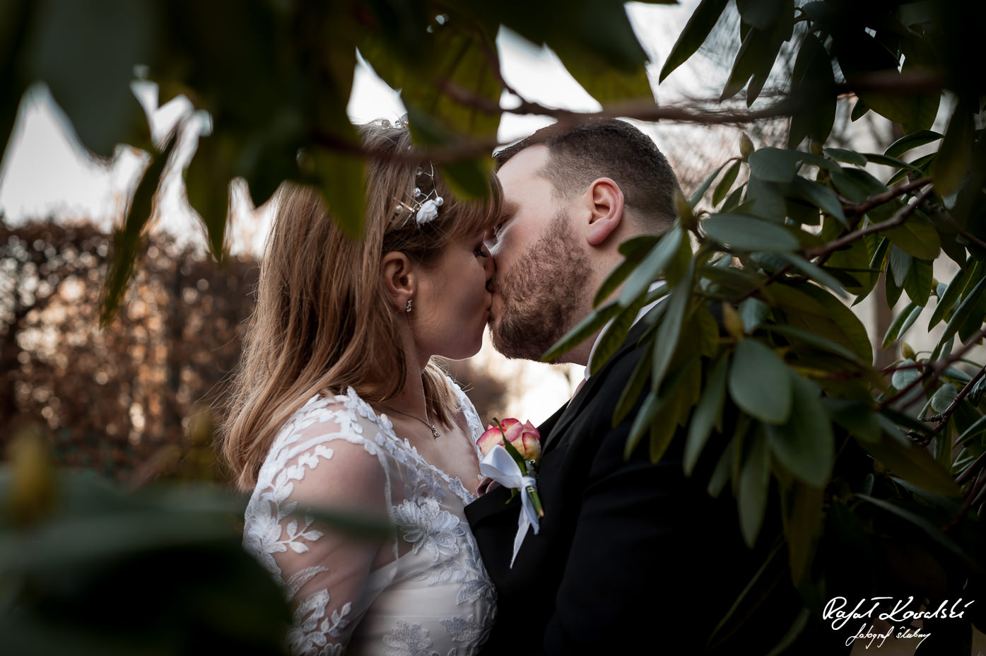 Plener Ślubny Gdynia - pocałunek młodej pary sfotografowany w prześwicie zielonych liści